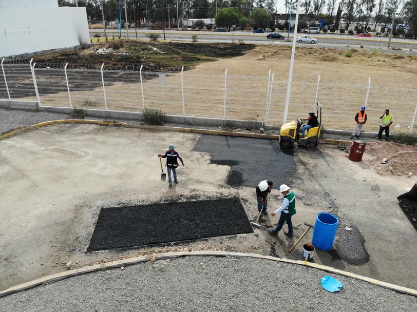 Cuadrilla haciendo bacheo con carpeta asfáltica y rodillo en patio industrial